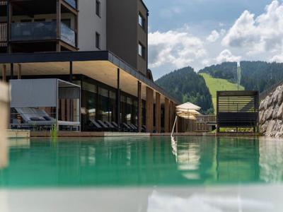 Moderner Hotelpool mit Bergblick und Sonnenschirmen an einem sonnigen Tag.