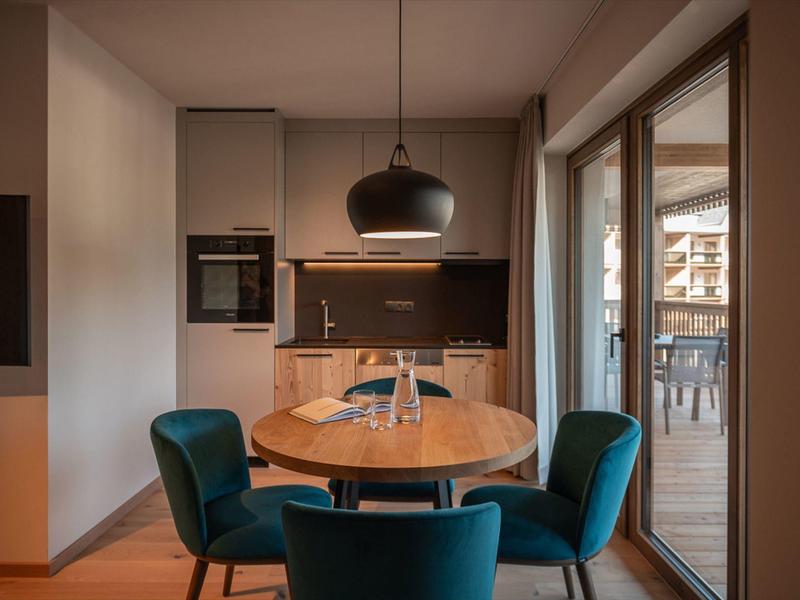 Cozy dining area with round wooden table, blue chairs, and modern kitchenette in natural light.