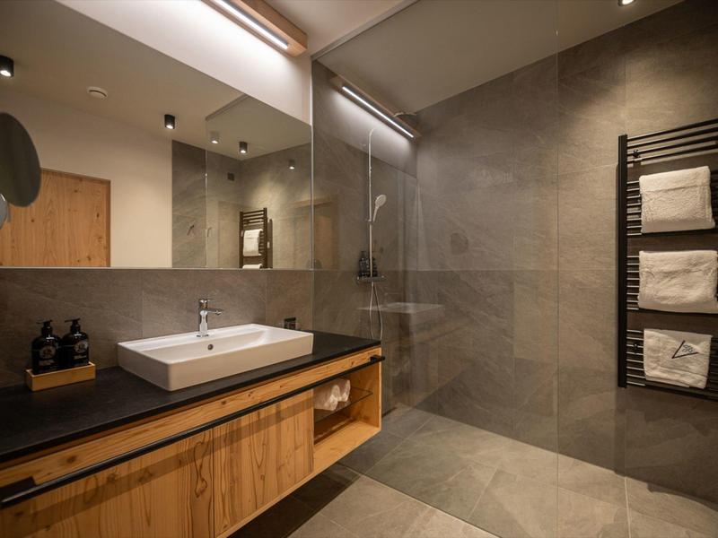 Modern bathroom with wooden vanity, large mirror, glass shower, and towel rack with towels.