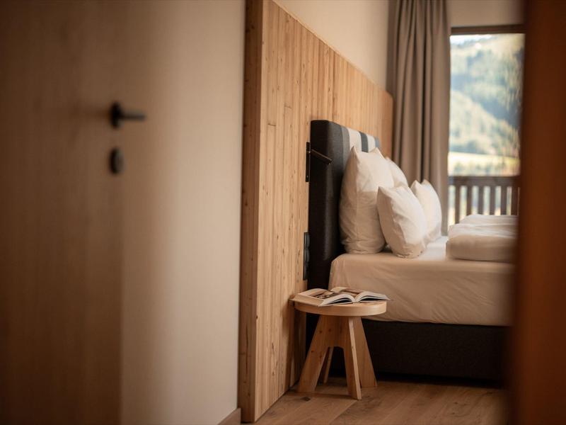 Cozy bedroom with wooden walls, white bedding, and a small wooden stool by the bed.