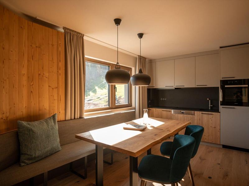 Cozy dining area with wooden walls, a window view, and modern hanging lights in a hotel room.