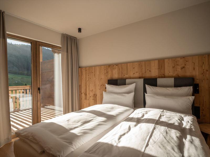 Cozy hotel room with twin beds, wooden headboard, and balcony with mountain view.