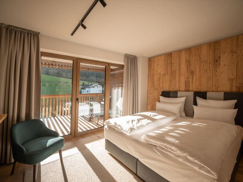 Cozy hotel room with double bed, wooden wall, balcony view, and natural light.