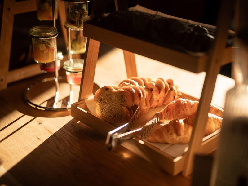 Warmly lit wooden table with sliced bread and jars nearby, creating a cozy breakfast scene.