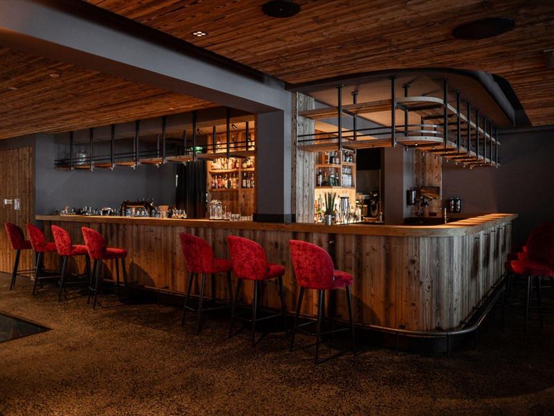 Cozy bar with wooden counter and red bar stools under warm wooden ceiling.