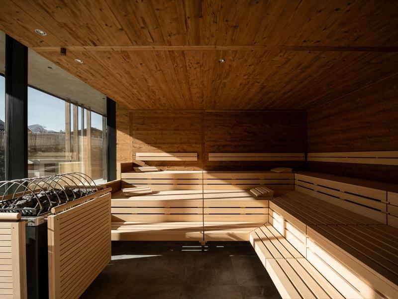 Interior of a wooden sauna with tiered benches and a heater by a window showing an outdoor view.