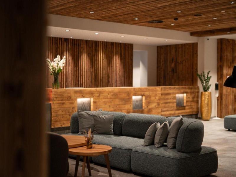 Cozy hotel lounge with wooden ceiling, reception desk, gray sofas, and warm lighting.