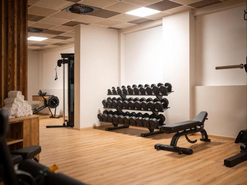 Gym room with dumbbell racks, bench, and exercise machines on wooden floor.