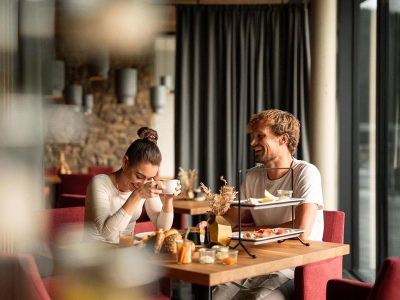 Couple enjoying drinks in a cozy restaurant with large windows and warm decor.