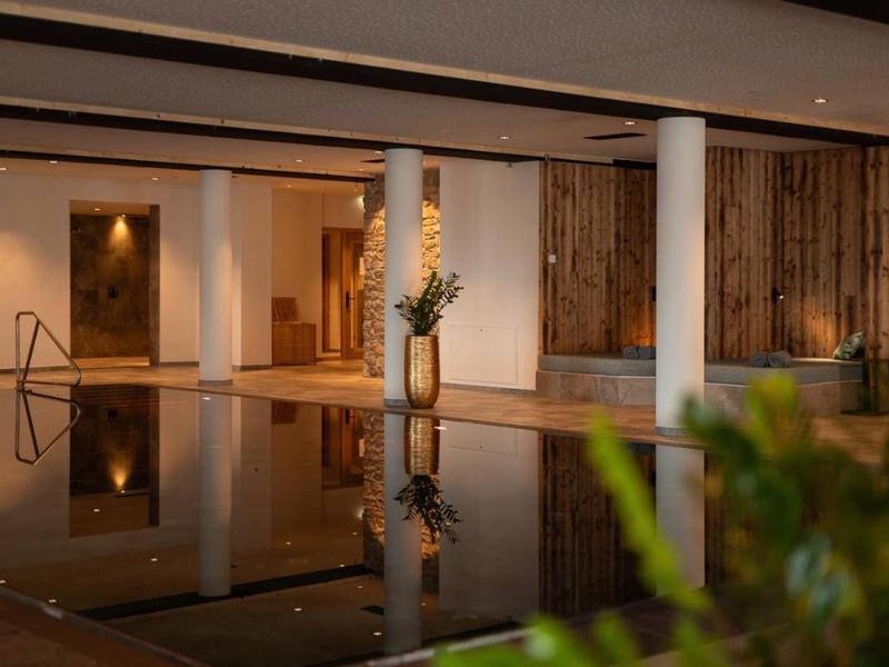 Modern indoor area with swimming pool, wooden decor, and columns in a hotel.