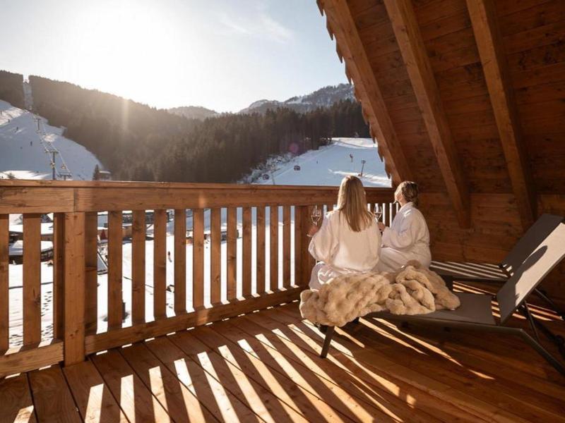 Two women in robes sit on a wooden balcony enjoying snowy mountain views.