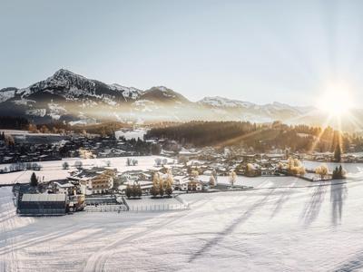 Paisaje montañoso nevado con un pueblo en el valle y el sol brillando detrás de las montañas.