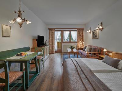 Habitación de hotel luminosa con cama doble, sofá, mesa de comedor y decoración rústica.