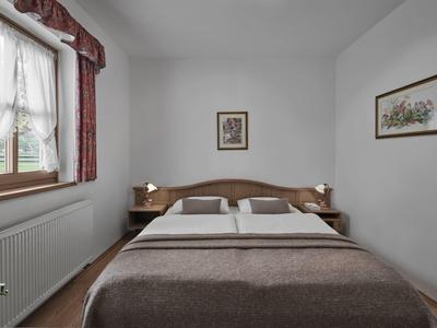 Dormitorio sencillo con cama doble, marco de madera y ventana con cortinas.