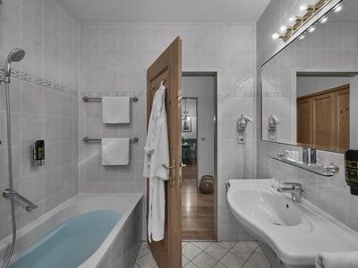 Baño moderno con bañera, lavabo, espejo grande y toallas en la pared.