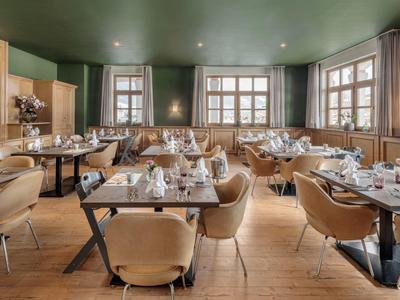 Helles Restaurant mit Holzboden, grünen Wänden, großen Fenstern und modernen braunen Stühlen.