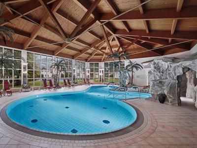 Vista interior de un hotel con piscina climatizada, jacuzzi y techo de vigas de madera.