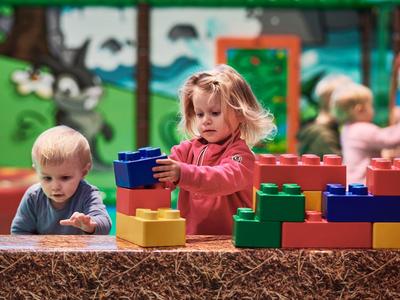 Niños juegan con bloques grandes y coloridos al aire libre frente a una pared pintada.