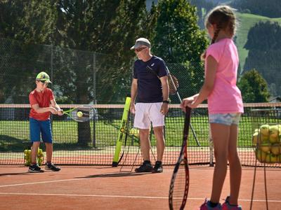 Tres personas en una cancha de tenis recogiendo pelotas y sosteniendo raquetas.
