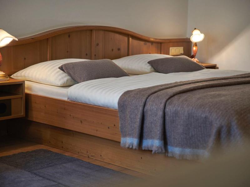 Cama doble acogedora con estructura de madera, sábanas blancas y mantas grises en habitación de hotel.