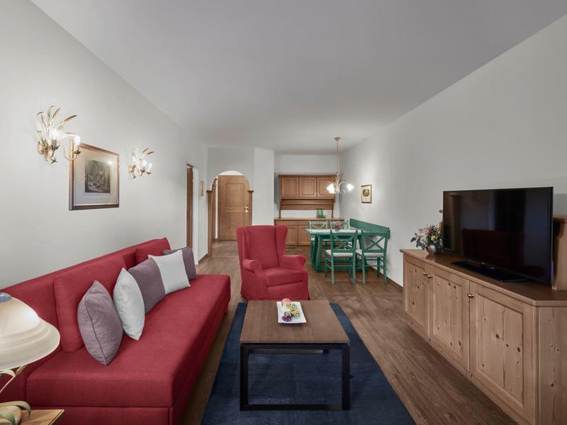 Sala acogedora con sofá rojo, televisor, muebles de madera y mesa de cocina al fondo.