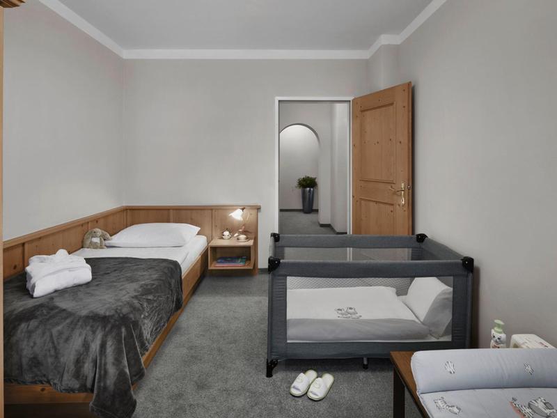 Habitación de hotel con dos camas individuales, cuna de bebé y decoración minimalista en tonos neutros.