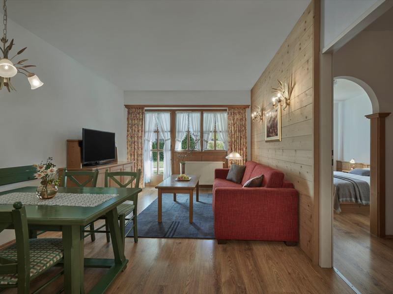 Sala de estar con sofá rojo, mesa de comedor verde y ventana grande con vista al exterior.