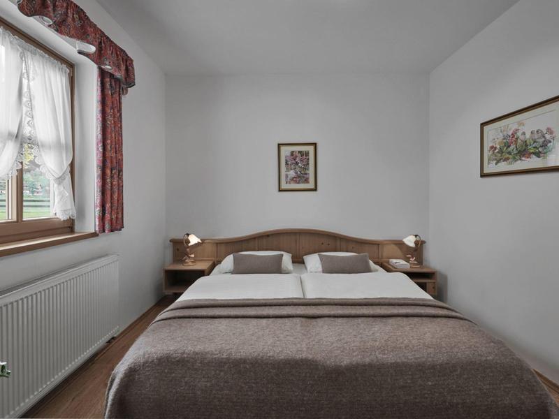 Dormitorio sencillo con cama doble, marco de madera y ventana con cortinas.