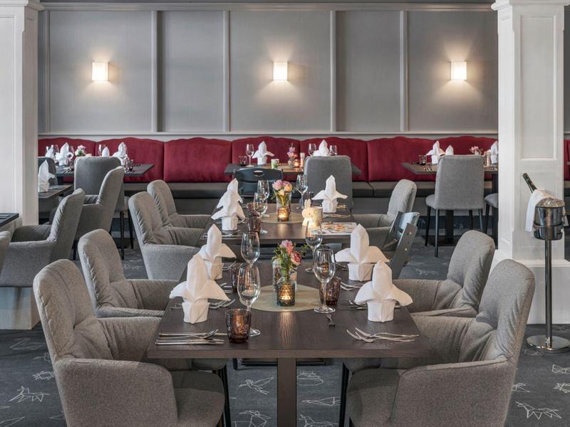 Restaurante elegante con mesas bien puestas y sillones tapizados grises en un hotel.