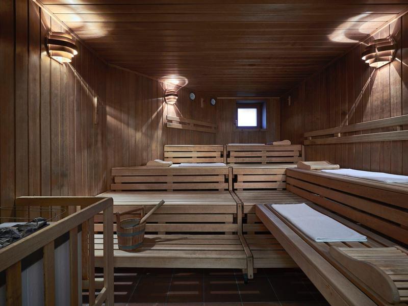 Interior de una sauna de madera con bancos en varios niveles y luces tenues.