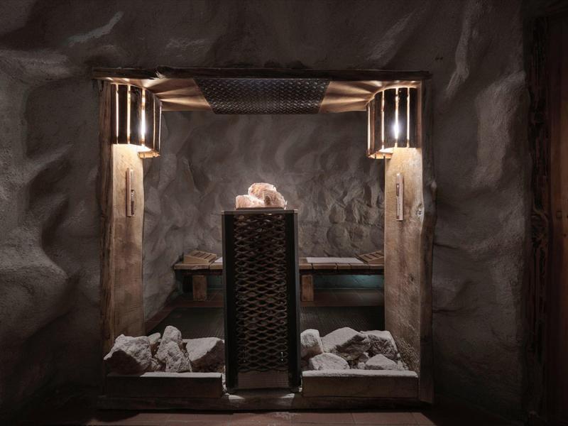 Sauna con paredes de piedra, luz tenue y piedras calientes en el centro para relajación