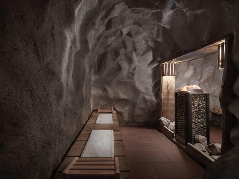 Pasillo rústico iluminado con paredes de piedra y bancos de madera junto a espejos grandes.