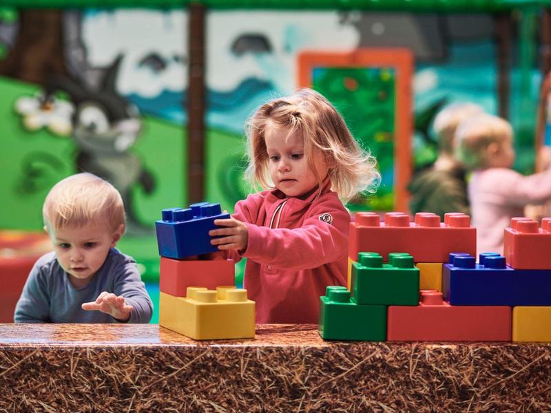 Niños juegan con bloques grandes y coloridos al aire libre frente a una pared pintada.