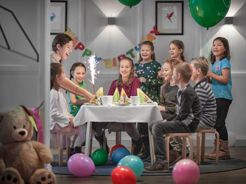 Niños celebran cumpleaños con globos y pastel en una habitación decorada festivamente.