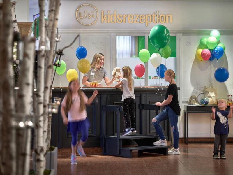 Niños juegan con globos de colores en la recepción del hotel con interiores modernos y claros.