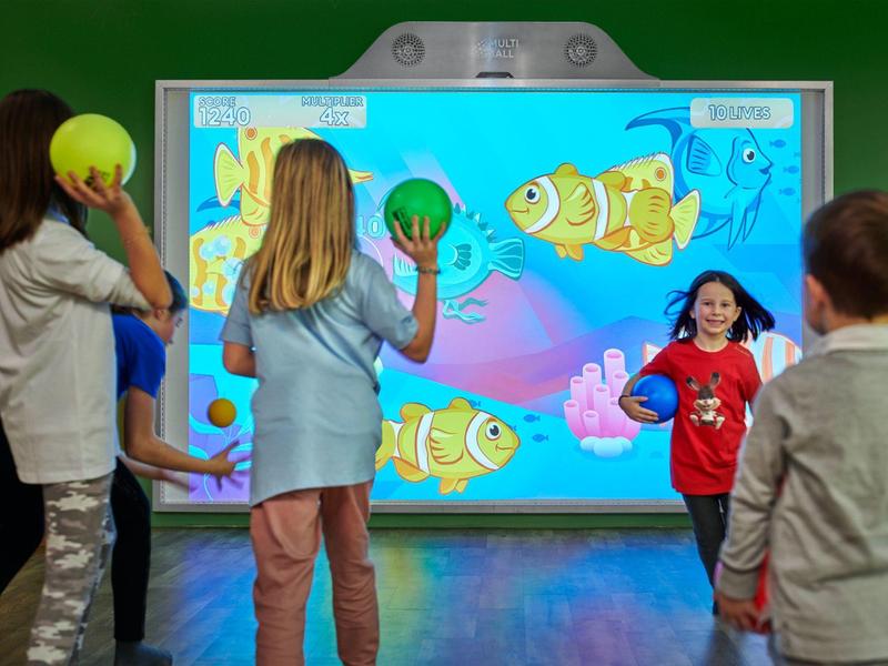 Niños juegan interactivamente con una pared temática submarina en la sala de ocio.