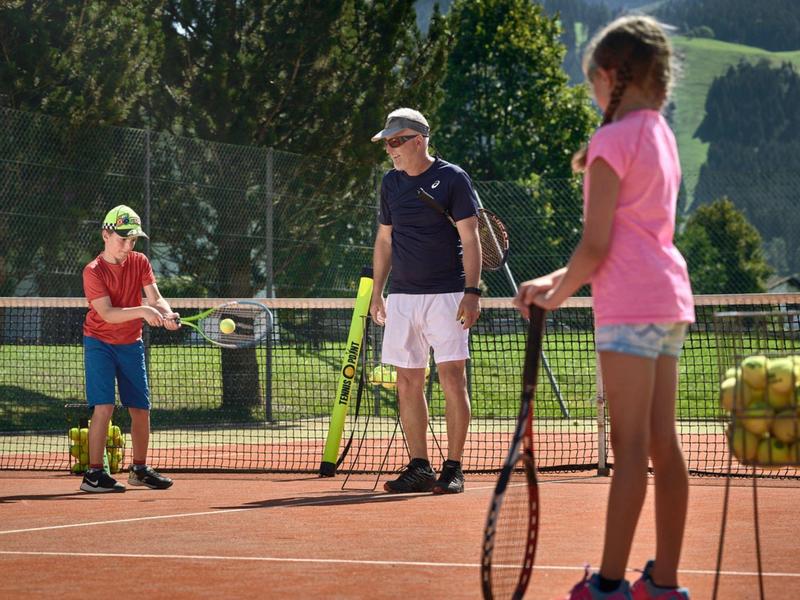 Tres personas en una cancha de tenis recogiendo pelotas y sosteniendo raquetas.