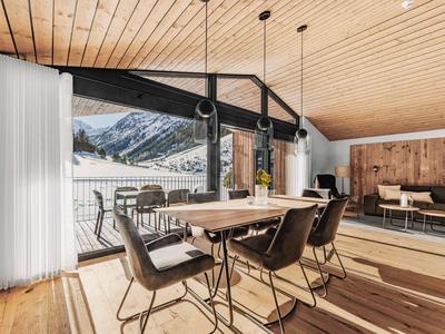 Moderner Essbereich mit Holztisch, schwarzen Stühlen, großen Fenstern und Bergblick, Holzdecke und Wand.