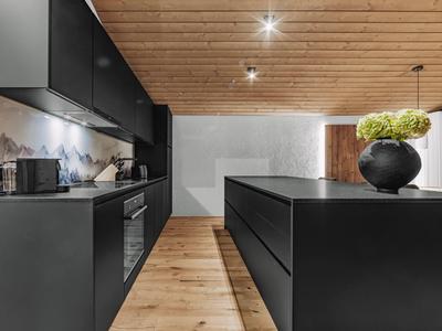 Cocina moderna con armarios negros, suelo de madera y techo de madera con iluminación.