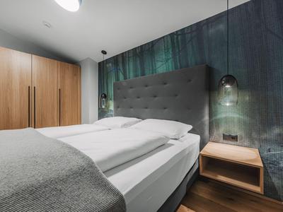 Dormitorio moderno con cabecero gris, muebles de madera y diseño de pared verde.