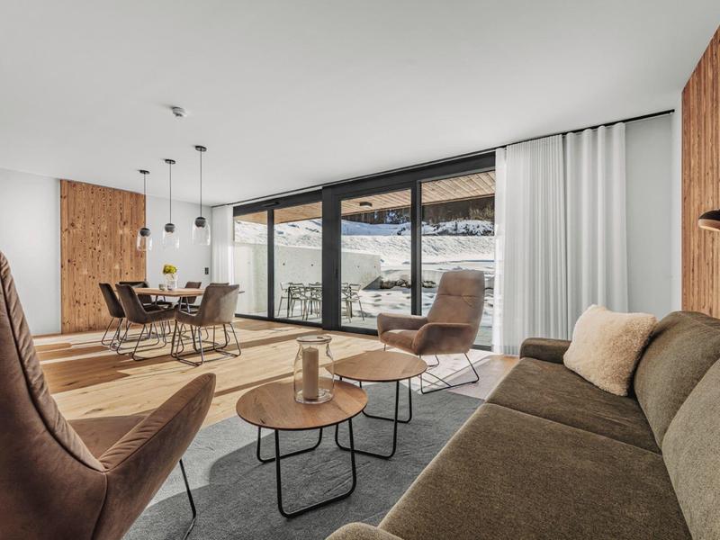 Modern ingerichte woonkamer met grote ramen en uitzicht op besneeuwde bergen.