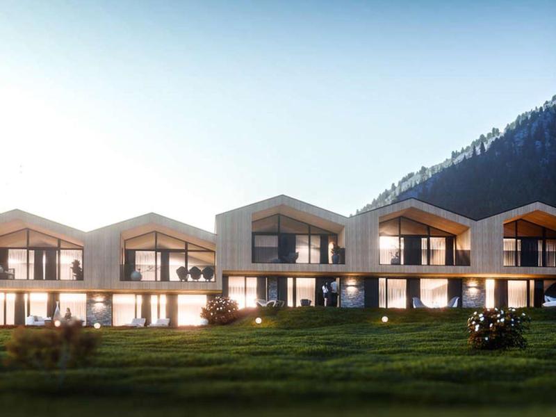 Moderne rijtjeshuizen met grote ramen en balkons met bergen op de achtergrond bij zonsondergang.