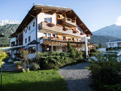 Großes weißes Alpenhaus mit Holzelementen, Balkonblumen und Garten vor Berglandschaft.