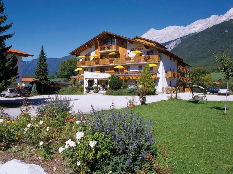 Tradycyjny hotel chalet z kwiatami na balkonach, górskim tłem i zadbanym ogrodem.