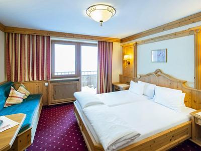 Lichte hotelkamer met tweepersoonsbed, blauwe bank, tapijtvloer en houten lambrisering.