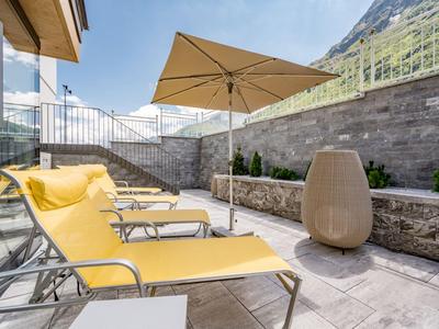 Gelbe Liegestühle und Sonnenschirm auf einer sonnigen Terrasse mit Bergblick.