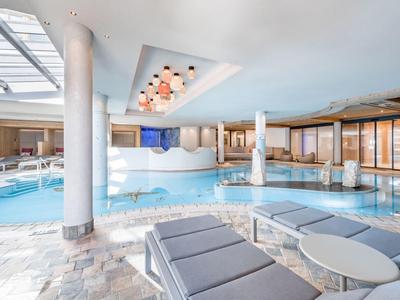 Helder verlicht binnenzwembad met ligstoelen en modern design in een hotel.