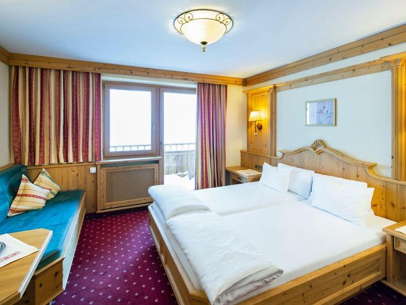 Lichte hotelkamer met tweepersoonsbed, blauwe bank, tapijtvloer en houten lambrisering.