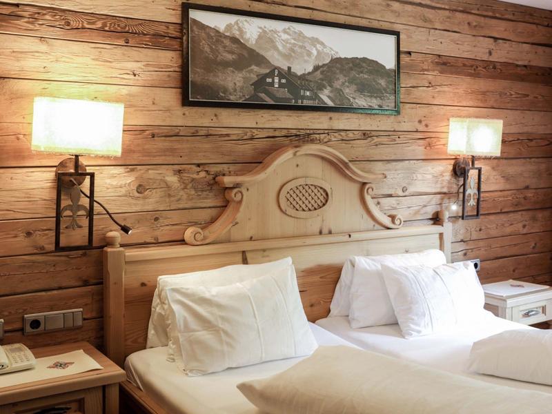 Gezellige hotelkamer met houten wandpanelen, tweepersoonsbed, nachtkastjes en bergfoto aan de muur.