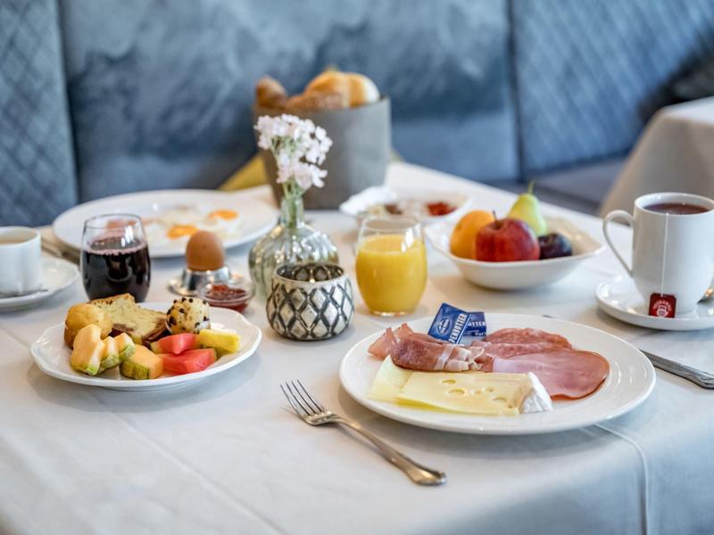 Tafel met ontbijtgerecht, koffie, sap en vers fruit in een hotel met een blauwe achtergrond.